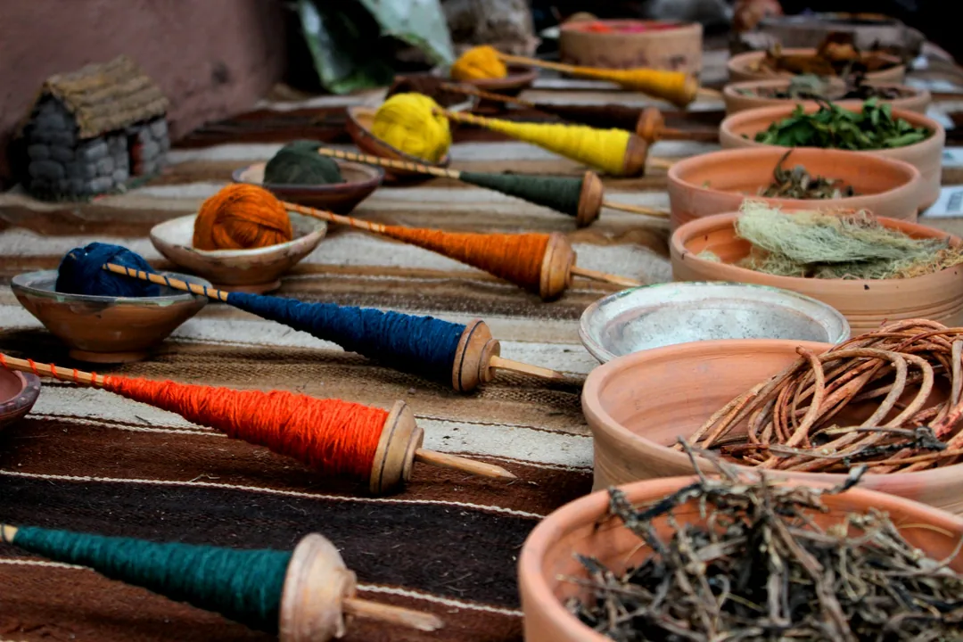 Madejas de hilo teñidas con colorantes vegetales junto a cuencos con materia tintórea seca